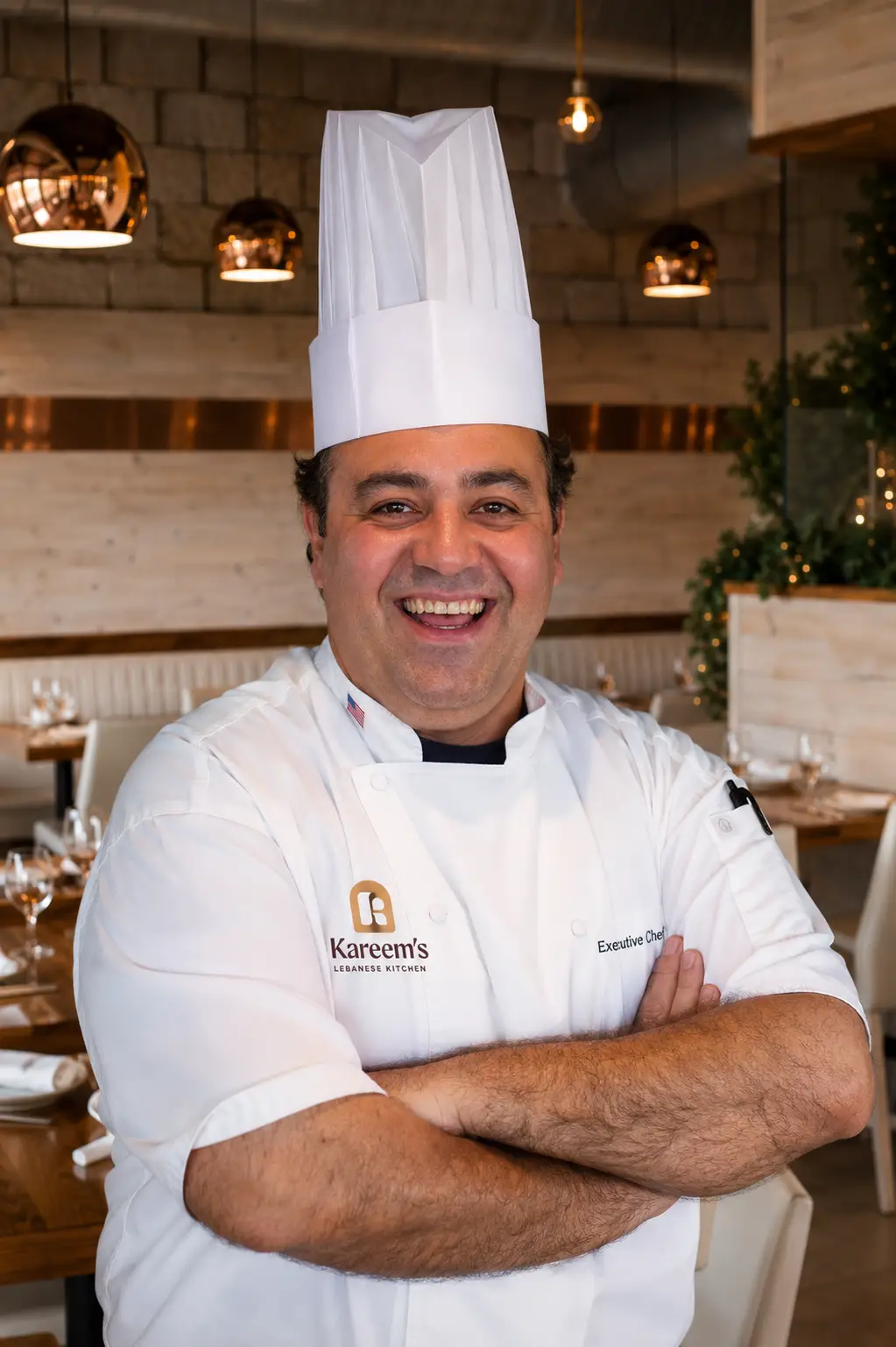 Executive Chef Rachid Hamdane stands proudly inside Kareem's Lebanese Kitchen, wearing a traditional chef's coat and hat, welcoming guests with a warm smile.