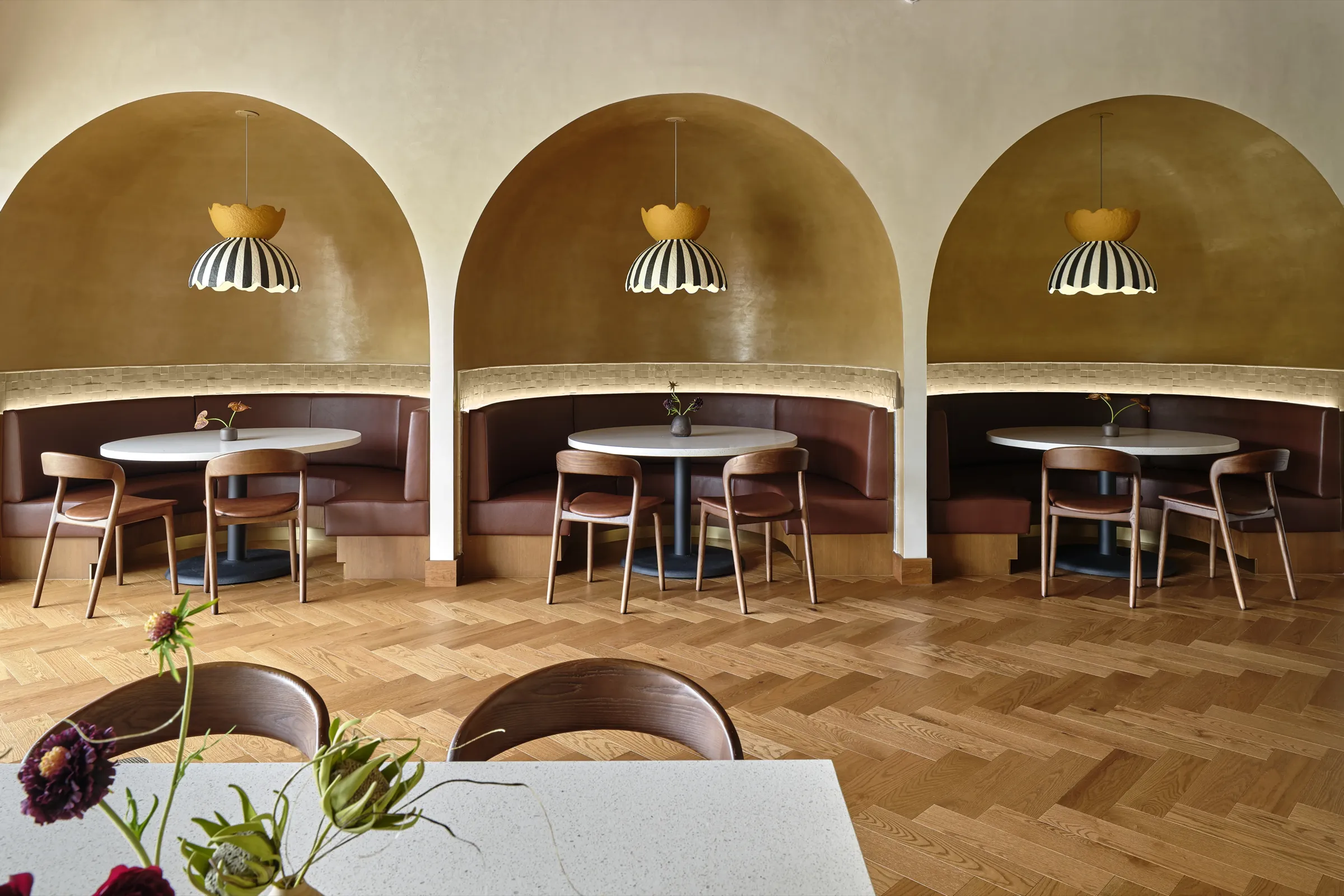 Gaithersburg dining room with three arched banquettes, round tables and striped pendant lights over a herringbone floor
