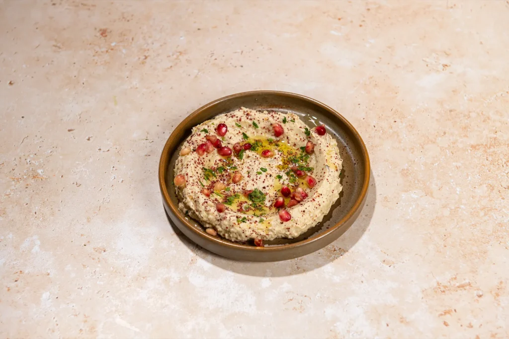 Smoky eggplant dip topped with pomegranate seeds, parsley, sumac and olive oil in a brown bowl