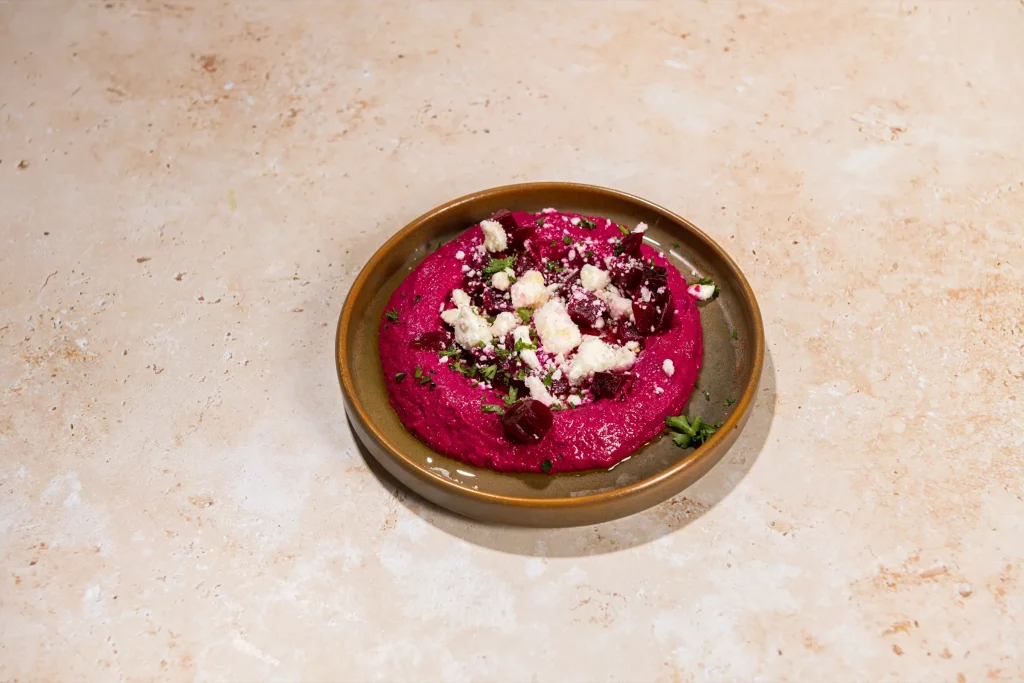 Bright magenta beet dip topped with crumbled white cheese, diced beets and parsley in a brown bowl