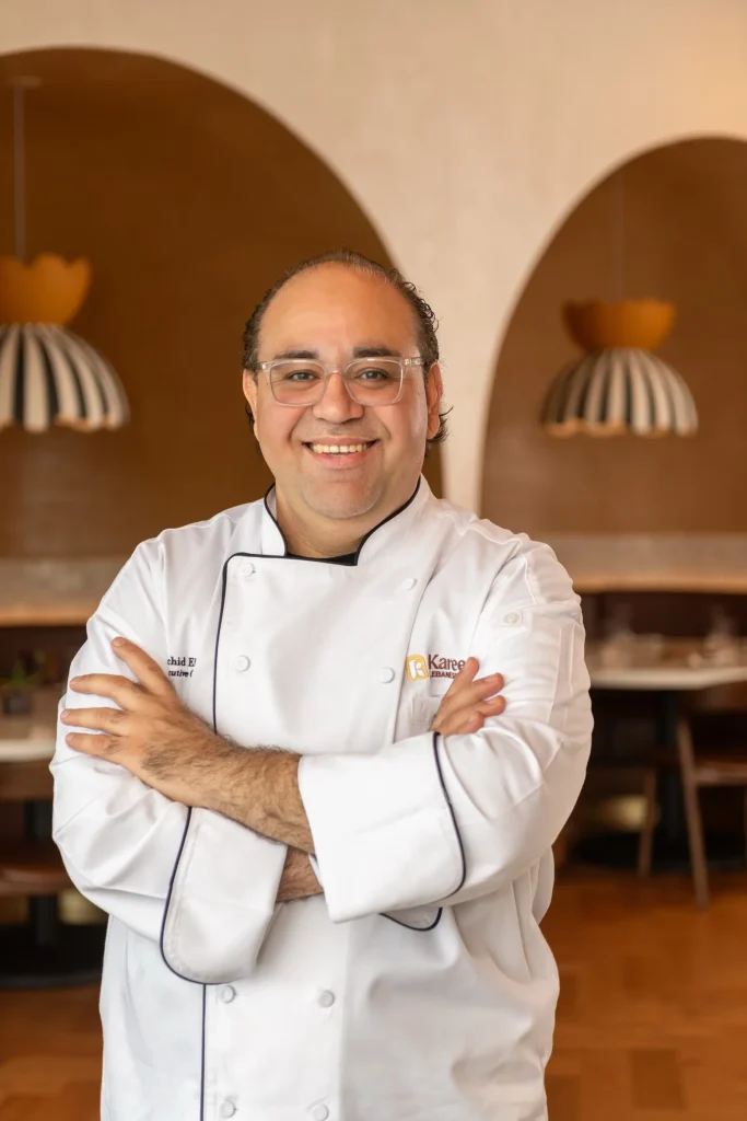 Chef Rachid Eido, smiling in a white jacket with arms crossed in the dining room