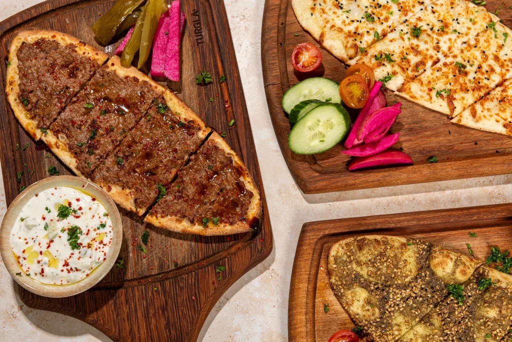 Meat flatbread with yogurt dip, cheese and za'atar flatbreads, pickles and vegetables on wooden boards