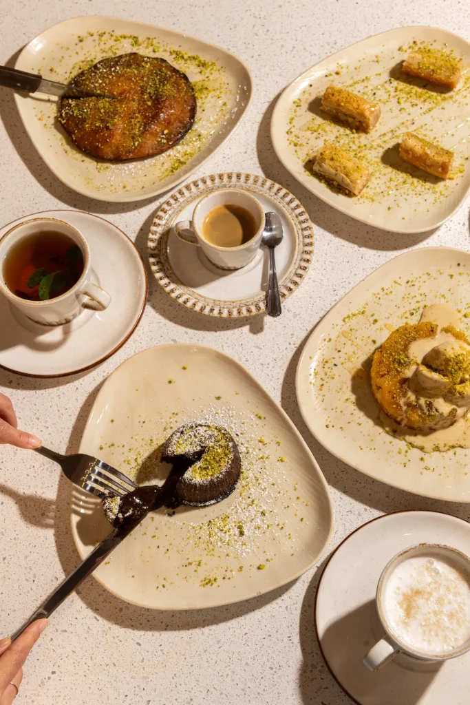 Knafeh, baklava, a chocolate lava cake being cut and a cream-topped dessert with tea, coffee and a latte