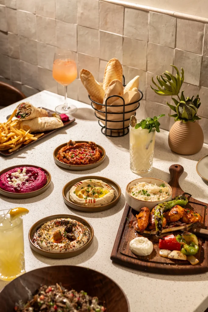 Table with hummus, muhammara, beet dip, labneh, shawarma wraps with fries, grilled chicken skewers, pita and drinks