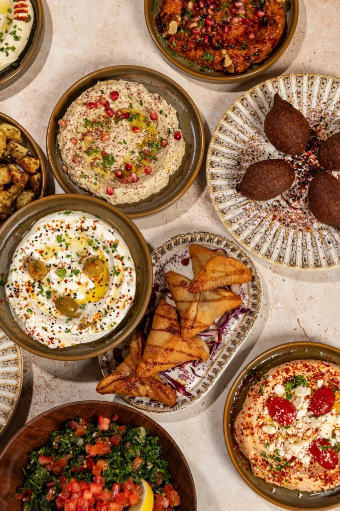 Overhead mezze of kibbeh, labneh with olives, muhammara, pastry triangles, tabbouleh and hummus with feta