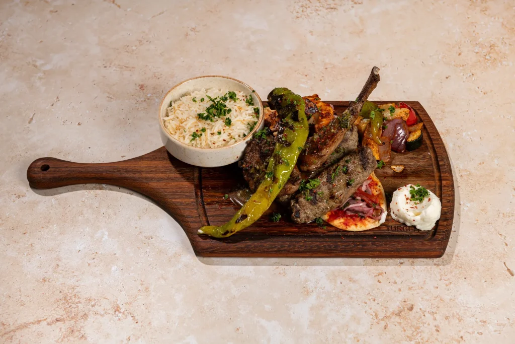 Mixed grill with lamb chop, kafta, chicken, blistered pepper, roasted vegetables, rice and white dip on a paddle board