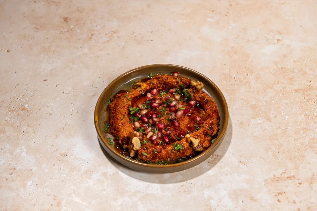 Red pepper and walnut dip topped with pomegranate seeds, walnut halves, parsley and pomegranate molasses