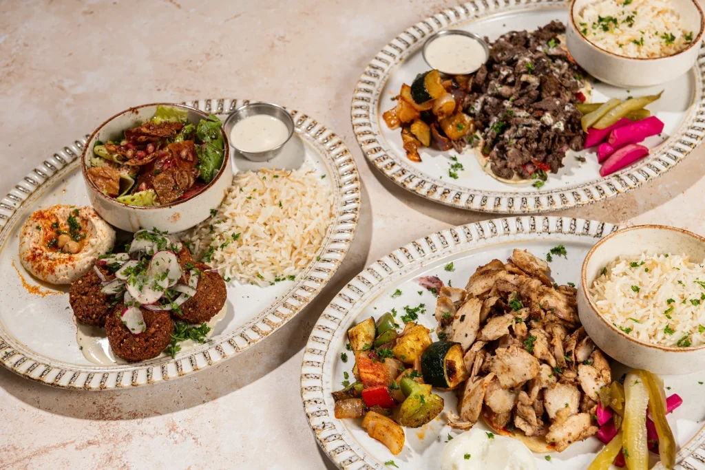 Three plates: falafel with hummus and fattoush, beef shawarma with pickles, and chicken shawarma with rice and vegetables