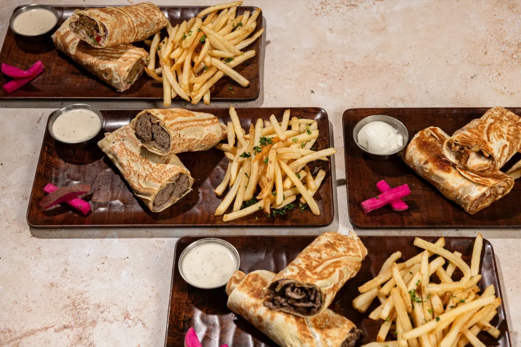 Four trays of grilled wraps with fries, pickled turnips and garlic sauces on a stone tabletop